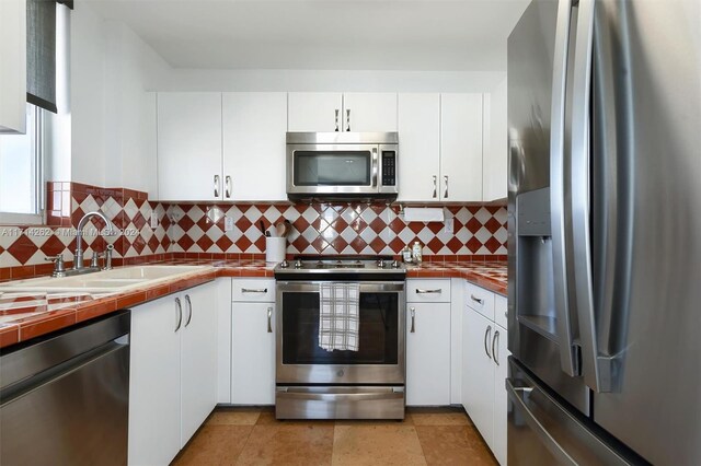 kitchen featuring white cabinets, tile counters, sink, and stainless steel appliances