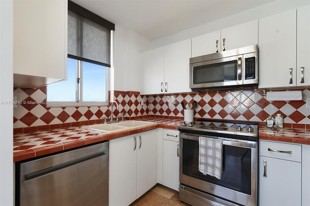 kitchen featuring tile countertops, sink, white cabinets, and appliances with stainless steel finishes