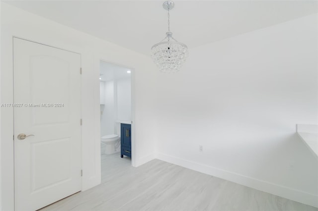 empty room featuring a notable chandelier and light wood-type flooring