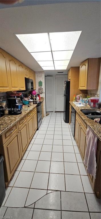 kitchen with light tile patterned floors, light stone counters, and black appliances