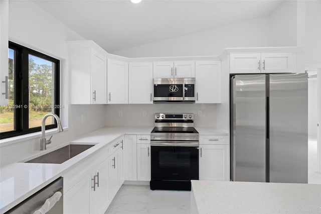 kitchen featuring stainless steel appliances, a sink, lofted ceiling, white cabinetry, and decorative backsplash