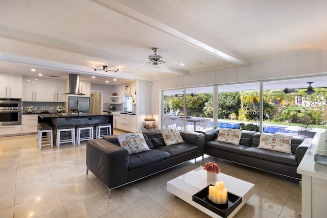 tiled living room with ceiling fan, sink, a textured ceiling, and beam ceiling