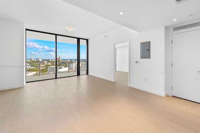 empty room featuring light wood-type flooring, electric panel, and expansive windows