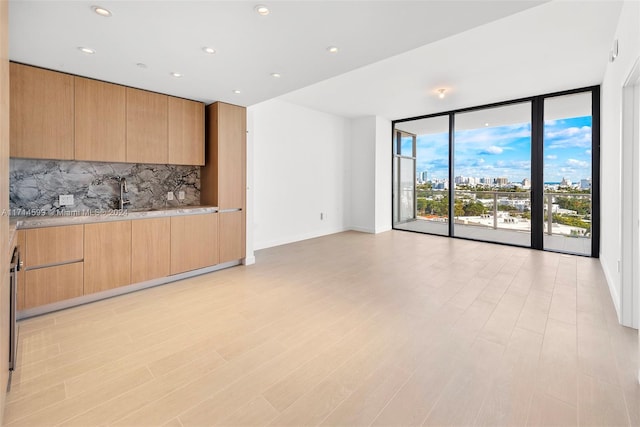 unfurnished living room featuring light hardwood / wood-style floors, a wall of windows, and sink