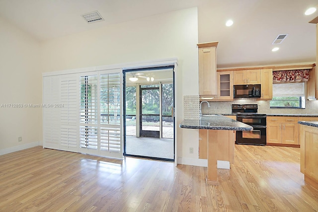 kitchen featuring a breakfast bar, light brown cabinets, dark stone counters, black appliances, and kitchen peninsula