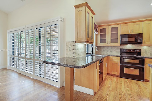 kitchen with kitchen peninsula, light wood-type flooring, sink, black appliances, and dark stone countertops