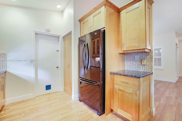 kitchen with light brown cabinets, light wood-type flooring, black fridge, and dark stone counters