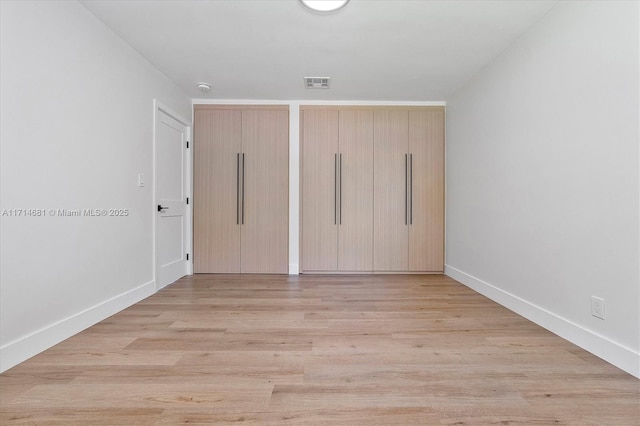 unfurnished bedroom featuring multiple closets and light hardwood / wood-style floors