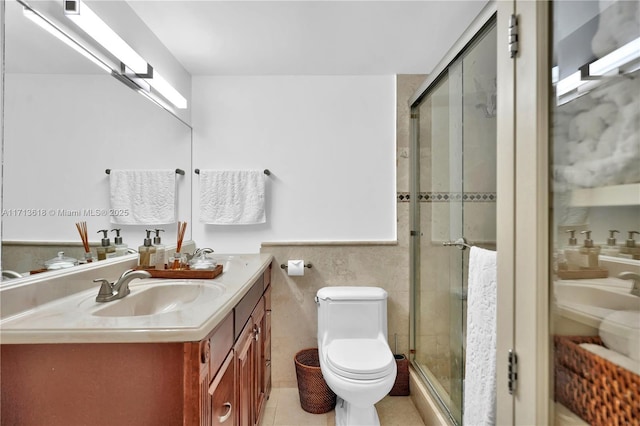 bathroom with tile walls, toilet, tile patterned floors, an enclosed shower, and vanity