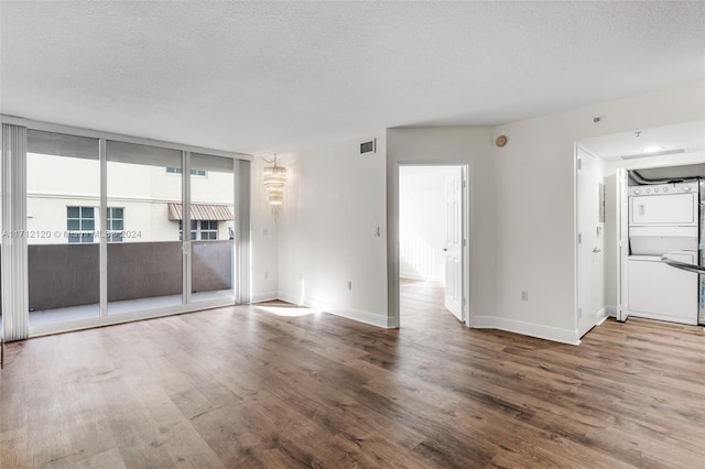 empty room featuring floor to ceiling windows, stacked washer and dryer, wood-type flooring, and a textured ceiling