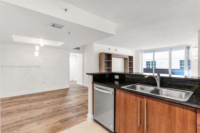 kitchen with a skylight, sink, stainless steel dishwasher, dark stone countertops, and light hardwood / wood-style floors