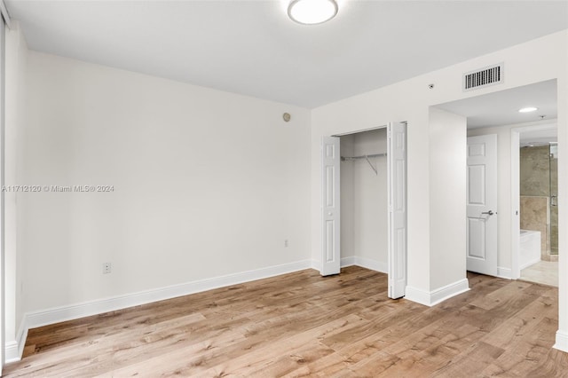 unfurnished bedroom featuring light wood-type flooring, connected bathroom, and a closet