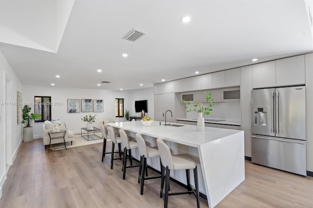 kitchen with a breakfast bar, a kitchen island with sink, white cabinets, light hardwood / wood-style flooring, and high quality fridge