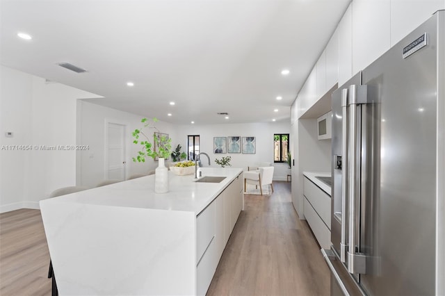 kitchen with sink, a spacious island, light hardwood / wood-style floors, high quality fridge, and white cabinets