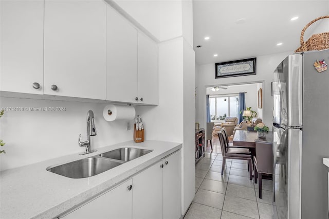 kitchen featuring ceiling fan, sink, white cabinetry, stainless steel refrigerator, and light tile patterned flooring