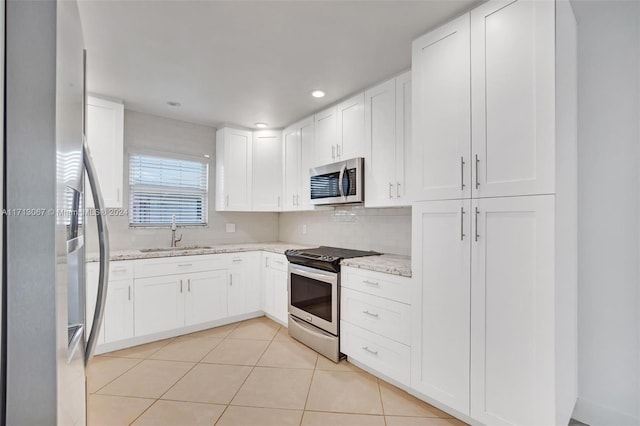 kitchen with sink, light tile patterned floors, appliances with stainless steel finishes, light stone counters, and white cabinetry