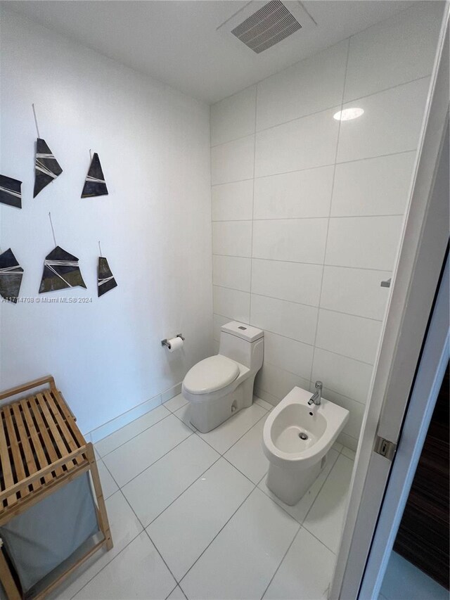 bathroom featuring tile patterned floors, toilet, tile walls, and a bidet