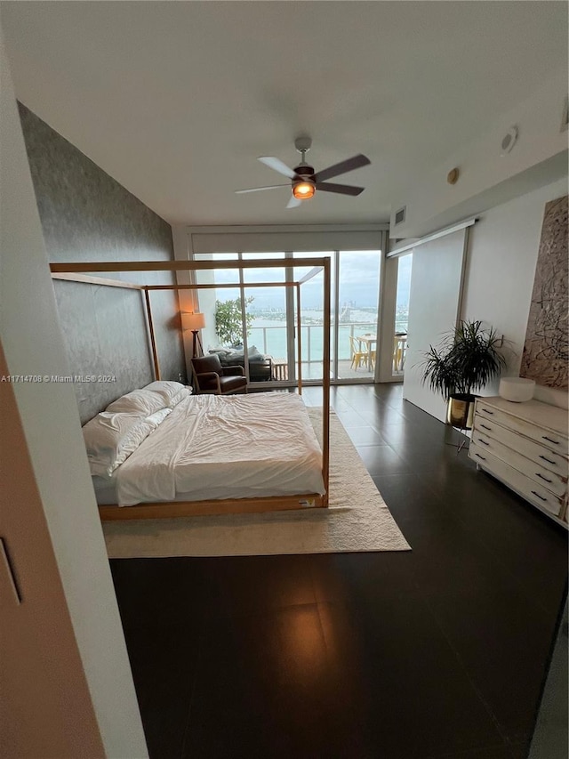 bedroom with access to exterior, ceiling fan, a water view, and a wall of windows