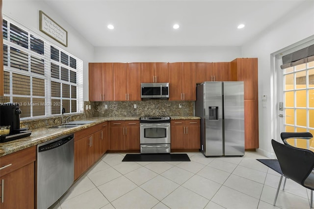 kitchen with sink, tasteful backsplash, light stone counters, light tile patterned flooring, and appliances with stainless steel finishes