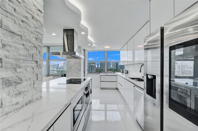 kitchen featuring white cabinets, wall chimney range hood, sink, light stone countertops, and stainless steel appliances