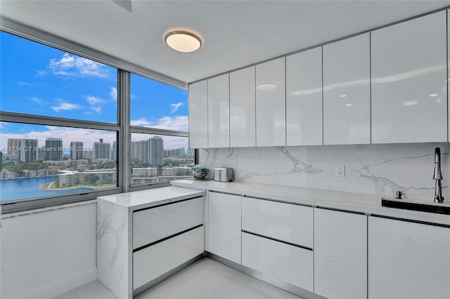 kitchen with white cabinetry, sink, light stone counters, backsplash, and a water view