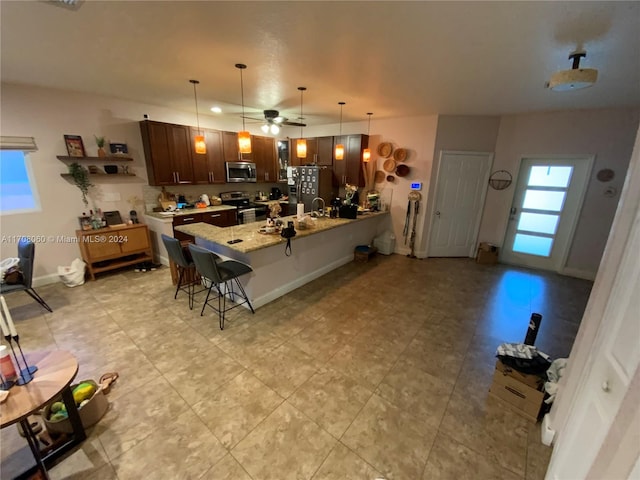 kitchen with ceiling fan, light stone countertops, stainless steel appliances, decorative light fixtures, and a kitchen bar