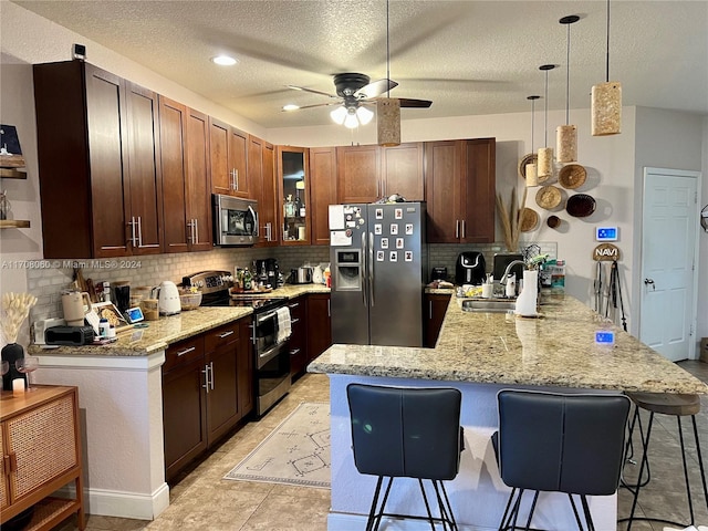 kitchen featuring kitchen peninsula, appliances with stainless steel finishes, ceiling fan, sink, and pendant lighting