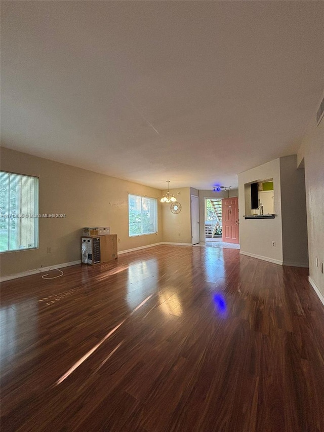 unfurnished living room with dark wood-type flooring and an inviting chandelier