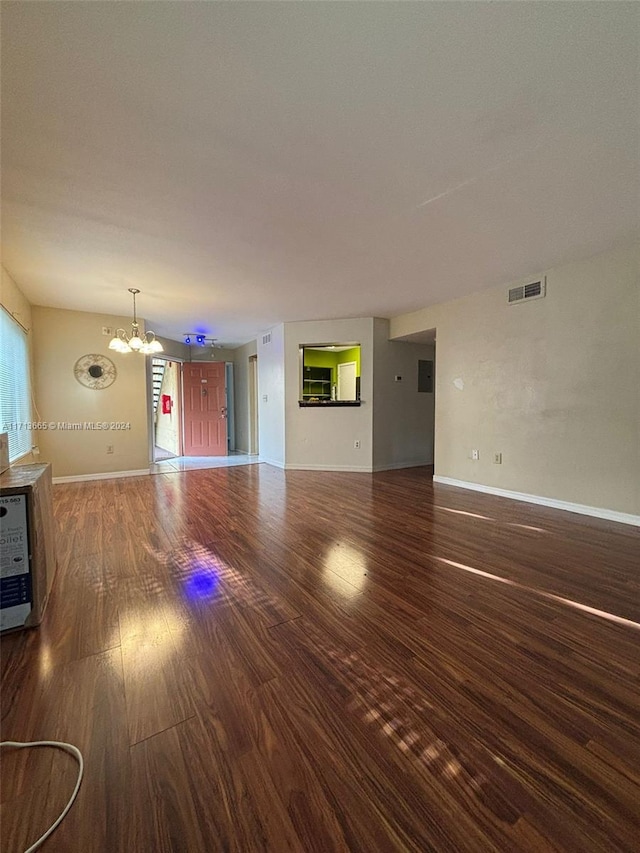 unfurnished living room with heating unit, dark hardwood / wood-style flooring, and an inviting chandelier