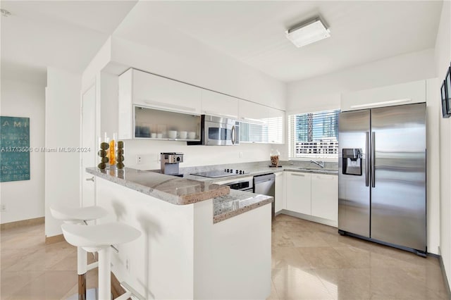 kitchen featuring white cabinetry, light stone countertops, a kitchen breakfast bar, kitchen peninsula, and appliances with stainless steel finishes