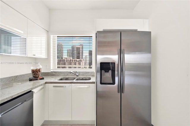 kitchen featuring appliances with stainless steel finishes, light stone counters, white cabinetry, and sink