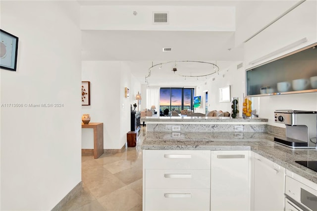 kitchen with wall oven, kitchen peninsula, white cabinetry, and light stone counters