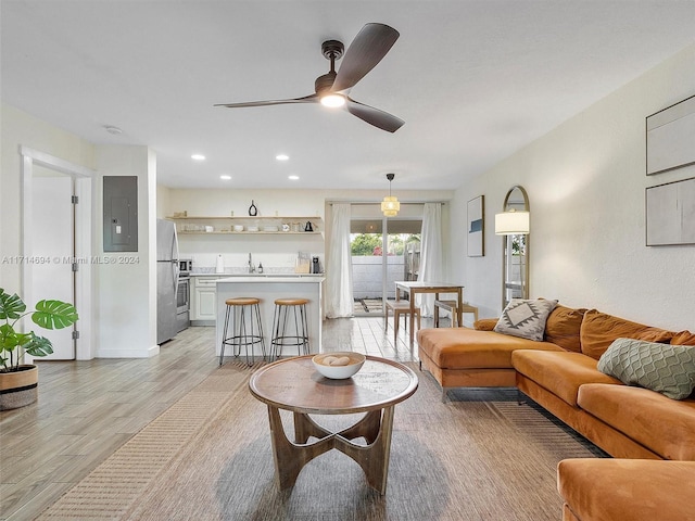 living room with ceiling fan, sink, electric panel, and light hardwood / wood-style flooring