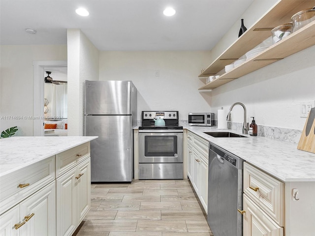 kitchen featuring light stone counters, ceiling fan, sink, and stainless steel appliances