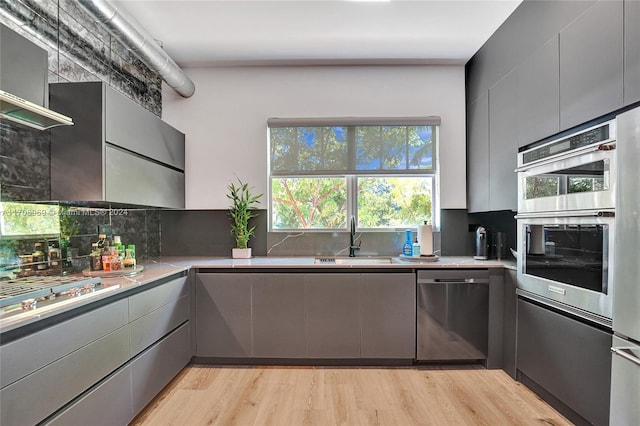 kitchen with decorative backsplash, appliances with stainless steel finishes, sink, light hardwood / wood-style flooring, and gray cabinets