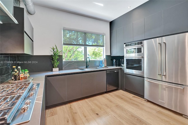 kitchen with backsplash, sink, light hardwood / wood-style floors, and appliances with stainless steel finishes