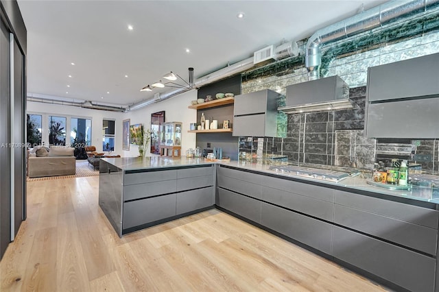 kitchen with gray cabinetry, stainless steel gas stovetop, light hardwood / wood-style floors, and kitchen peninsula