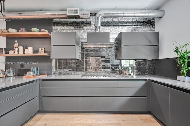 kitchen featuring backsplash, gray cabinetry, light hardwood / wood-style floors, and stainless steel gas cooktop