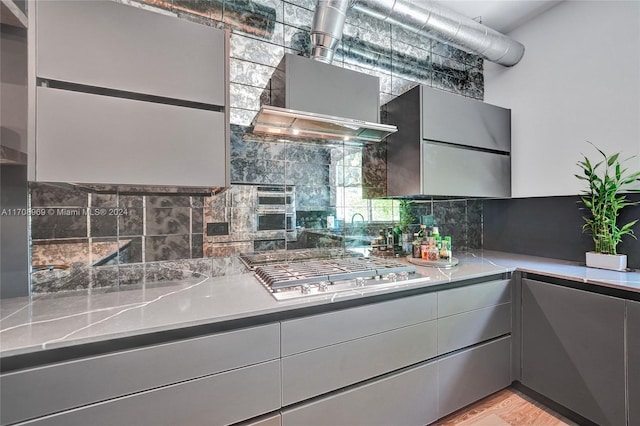 kitchen featuring backsplash, light stone counters, light hardwood / wood-style floors, gray cabinets, and stainless steel gas stovetop