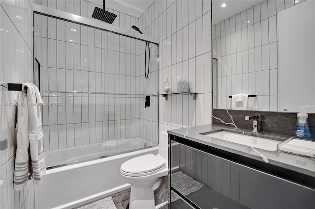 full bathroom with tile patterned floors, bath / shower combo with glass door, toilet, vanity, and tile walls