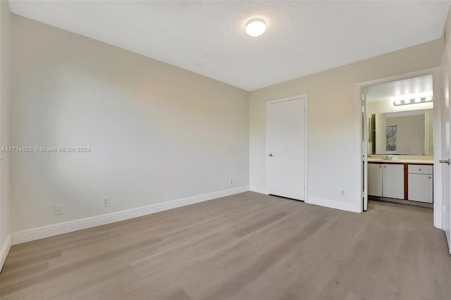 unfurnished bedroom featuring ensuite bathroom, a closet, light hardwood / wood-style floors, and a textured ceiling