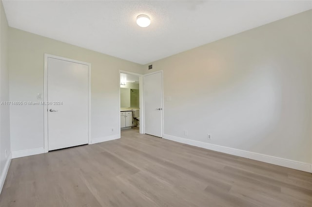 unfurnished bedroom featuring ensuite bathroom, light hardwood / wood-style flooring, and a textured ceiling