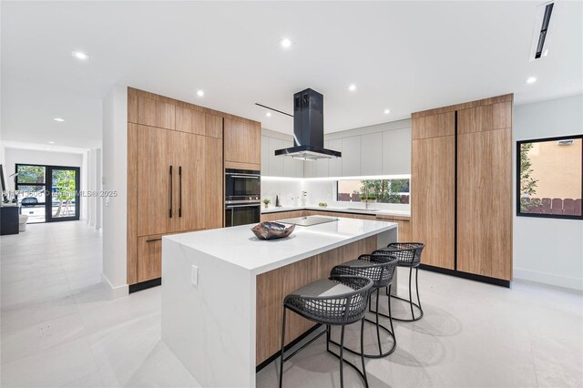 kitchen with a spacious island, island range hood, a kitchen breakfast bar, and black appliances