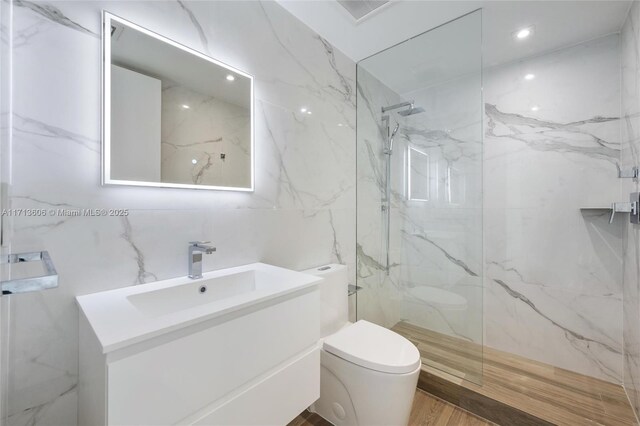 bathroom with tile walls, toilet, vanity, and a tile shower