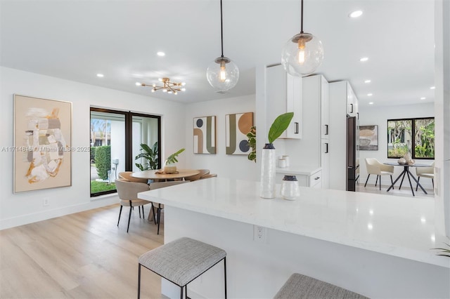 kitchen featuring stainless steel refrigerator, white cabinetry, hanging light fixtures, light stone counters, and kitchen peninsula