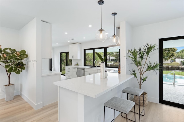 kitchen featuring pendant lighting, dishwasher, white cabinets, light hardwood / wood-style flooring, and kitchen peninsula