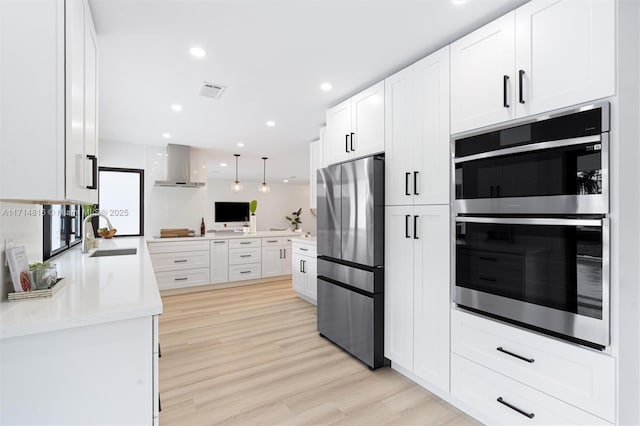 kitchen with sink, white cabinets, wall chimney range hood, and appliances with stainless steel finishes