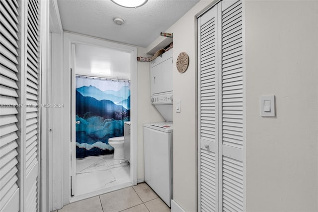 laundry room with a textured ceiling, light tile patterned floors, and stacked washer / drying machine