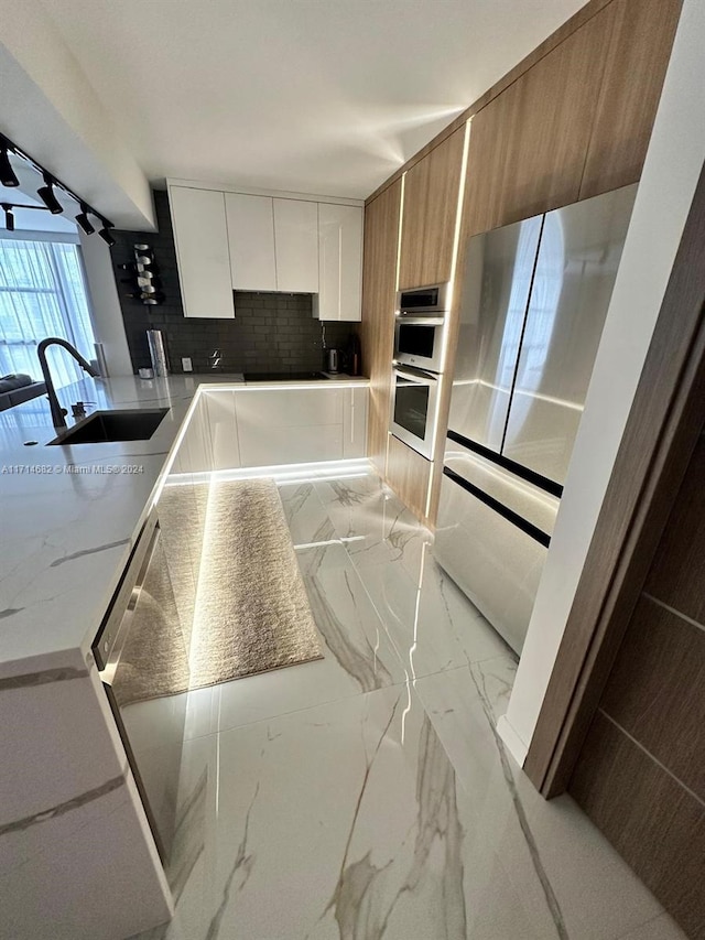 kitchen with white cabinets, sink, decorative backsplash, light stone countertops, and stainless steel double oven