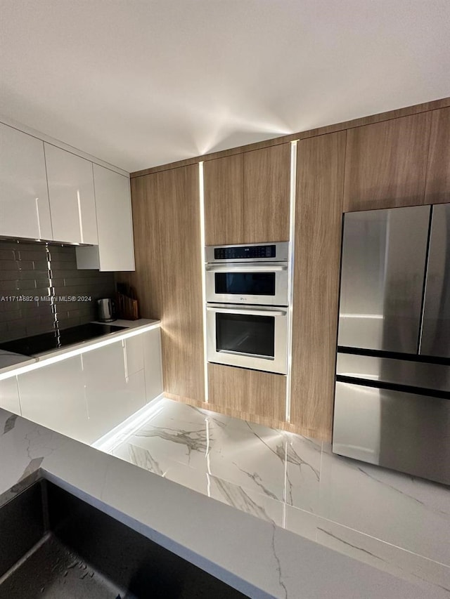 kitchen featuring white cabinets, appliances with stainless steel finishes, decorative backsplash, and light stone countertops